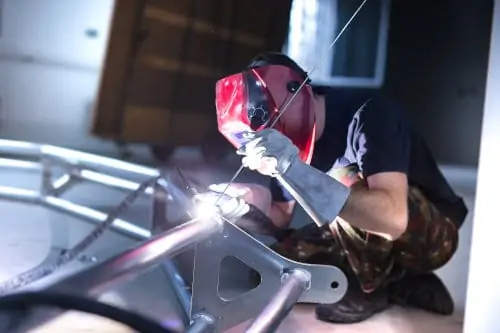 Man crouching on the ground TIG welding a large aluminum frame