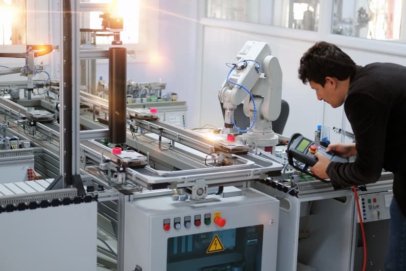 Man is holding a panel to control a robotic arm which is integrated on smart factory production line.